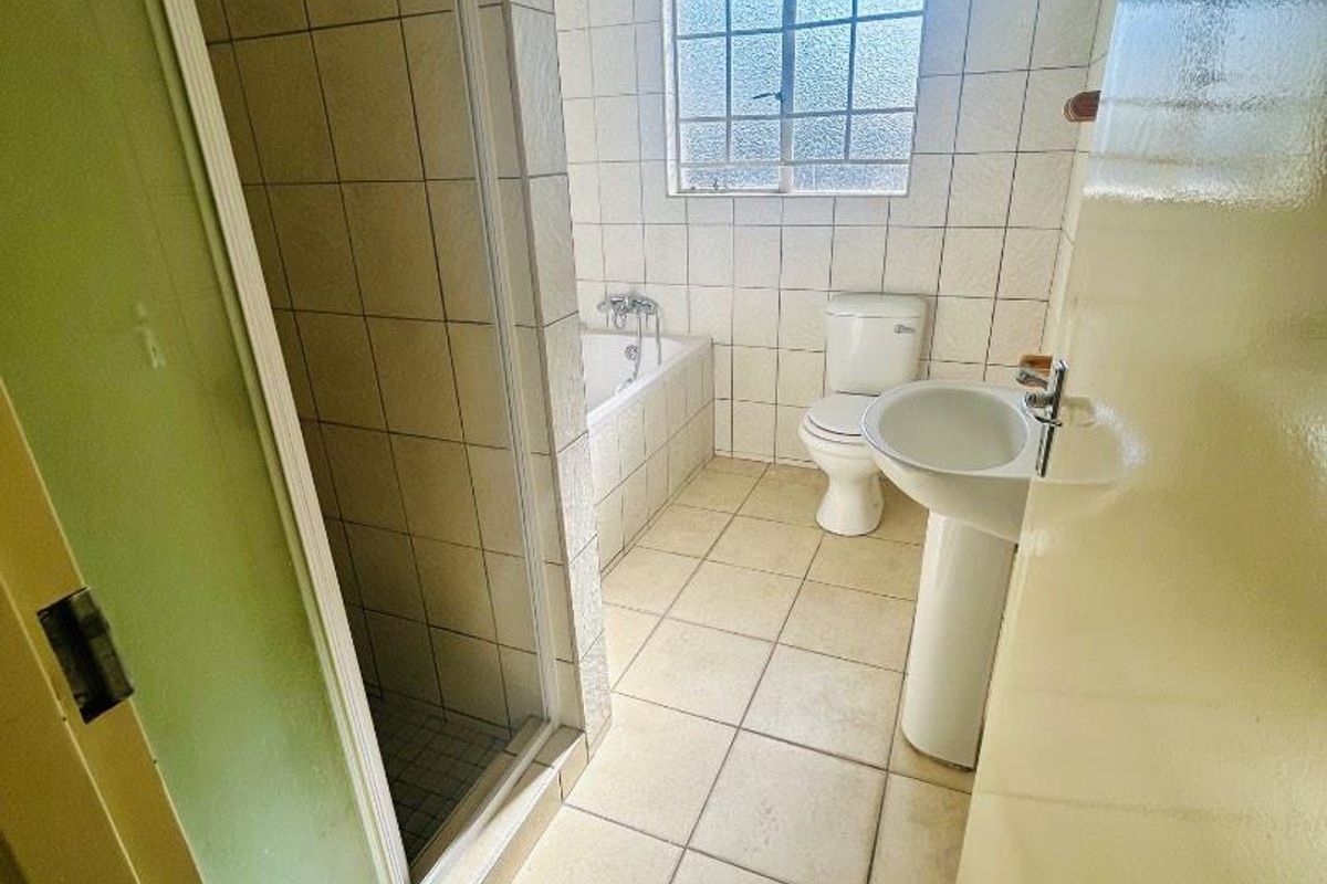 A functional bathroom featuring a separate shower enclosure, bathtub, pedestal sink, and toilet with neutral tiled finishes throughout.
