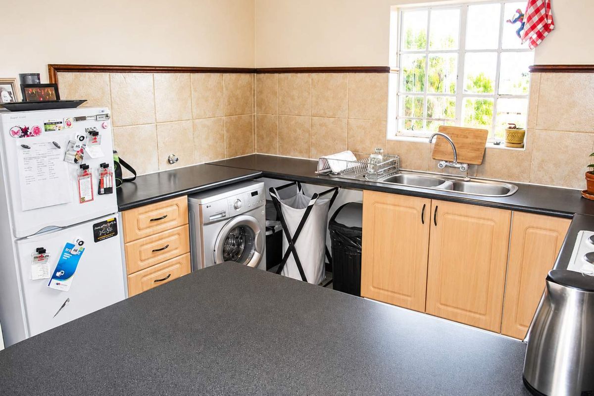 A functional kitchen featuring laminate cabinetry, dark countertops, a double bowl sink, and tiled splashbacks, providing a practical workspace with natural light.