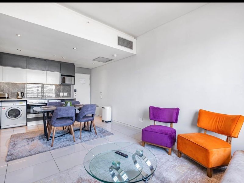Modern open-plan apartment featuring a sleek kitchen with integrated appliances, tiled flooring, and recessed lighting, seamlessly flowing into the living area.