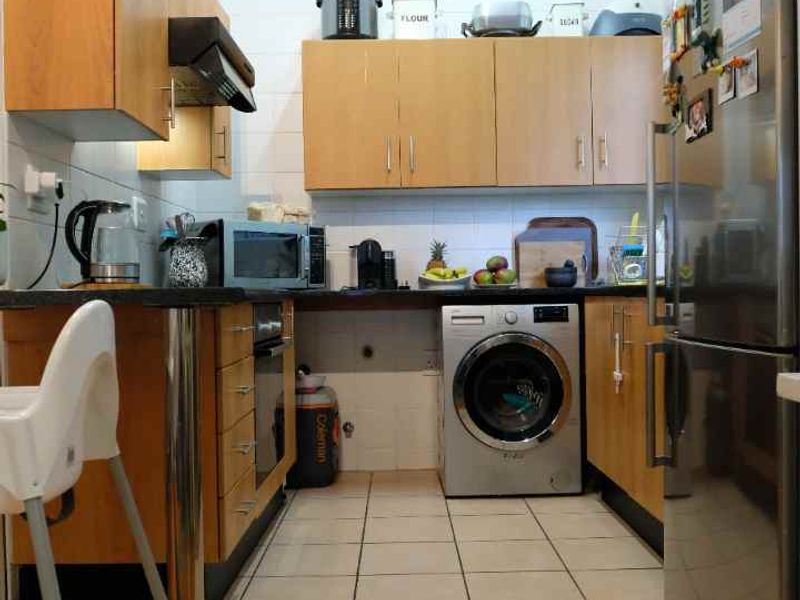 A functional galley-style kitchen featuring light wood-tone cabinetry, tiled flooring, and integrated laundry plumbing, offering a practical layout for apartment living.