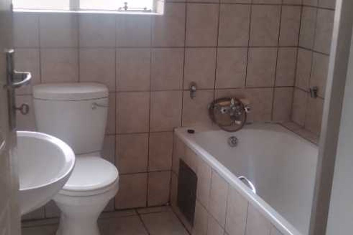 A functional bathroom featuring a bathtub, toilet, and pedestal basin with floor-to-ceiling wall tiling and a security-barred window.