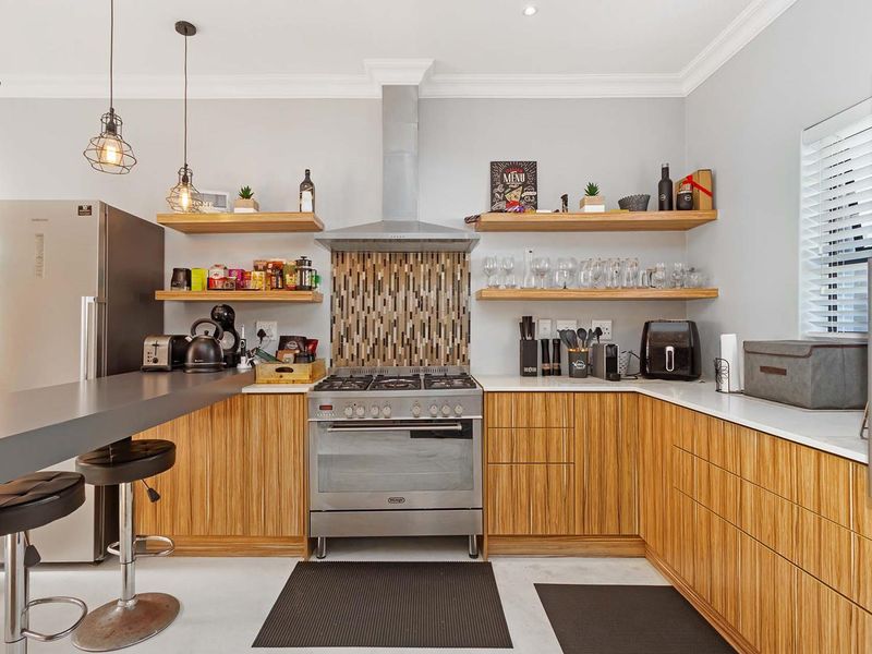 Modern kitchen featuring wood-grain cabinetry, stone countertops, a stainless steel gas stove with extractor fan, and floating shelving with a breakfast bar.