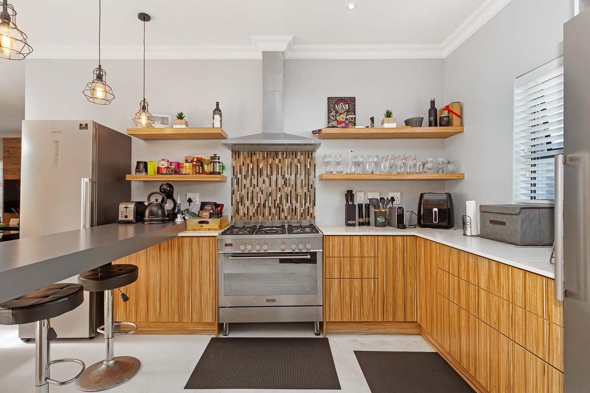 Modern kitchen featuring wood-grain cabinetry, stone countertops, a stainless steel gas stove with extractor fan, and floating shelving with a breakfast bar.