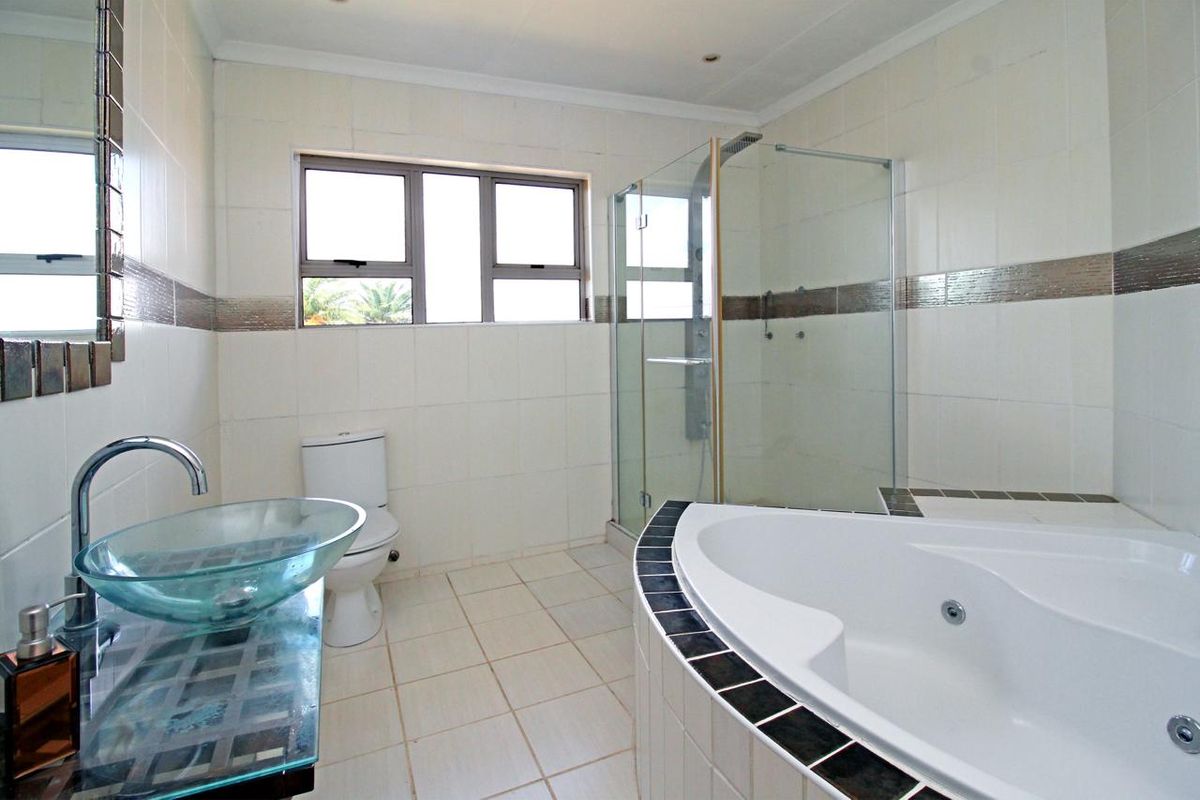 A spacious bathroom featuring a corner jetted bathtub, a glass-enclosed shower, and a modern glass vessel sink vanity.