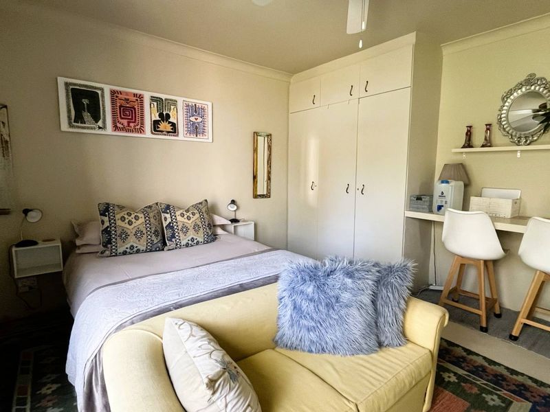 A functional bedroom featuring built-in cupboards, a ceiling fan, and a convenient integrated desk area, offering practical storage and workspace solutions.