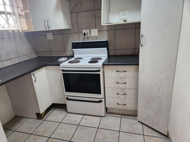 A functional kitchen featuring built-in cabinetry, laminate countertops, and a freestanding electric stove, with ceramic tiling throughout.