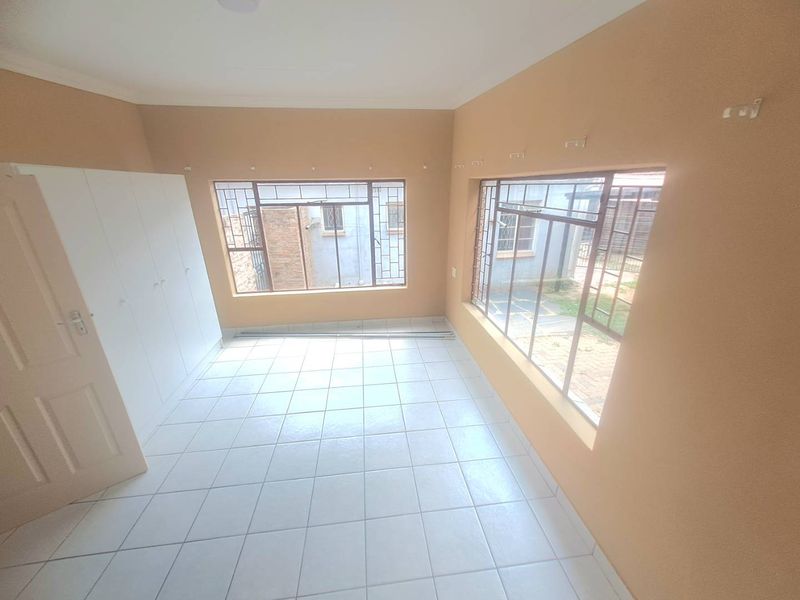 A bright, empty bedroom featuring tiled flooring, built-in cupboards, and large windows with security bars, offering a clean canvas for personalization.