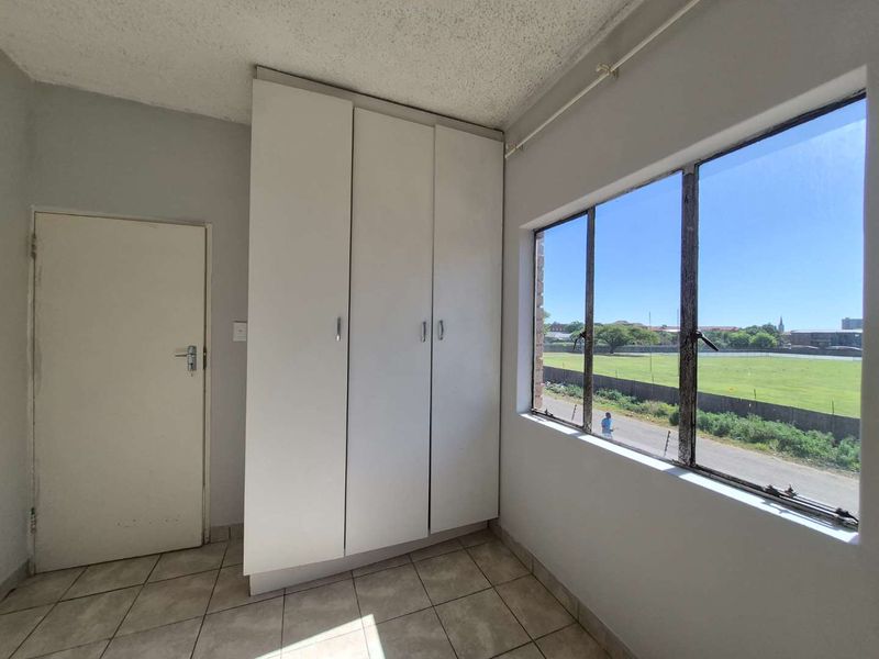 A vacant bedroom featuring built-in cupboards, tiled flooring, and large windows with views of the surrounding area.