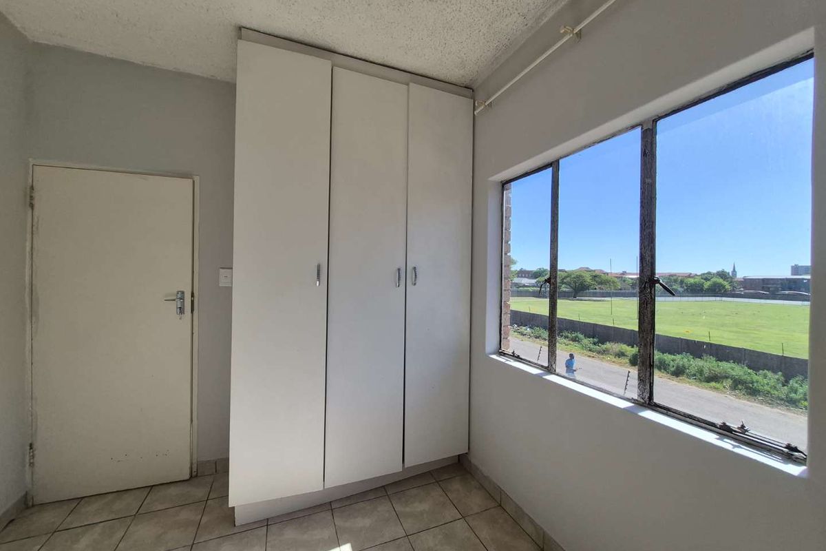 A vacant bedroom featuring built-in cupboards, tiled flooring, and large windows with views of the surrounding area.