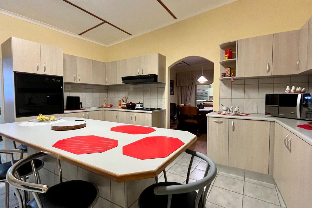 A functional kitchen featuring light wood-finish cabinetry, a central island, built-in oven, and tiled flooring, with an arched opening leading to the dining area.