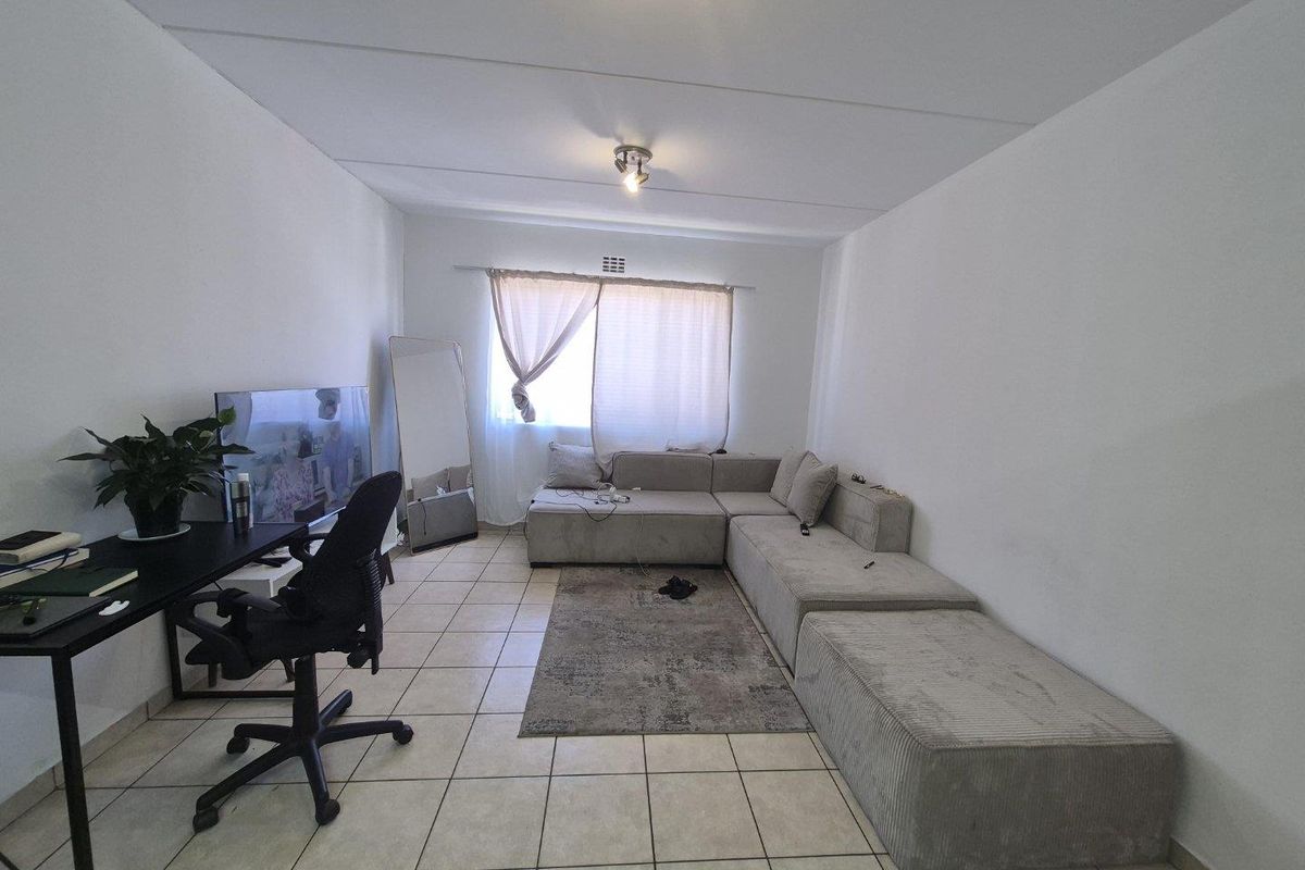 A functional living room featuring neutral tiled flooring and a ceiling light fixture, providing a versatile space for relaxation and home office use.