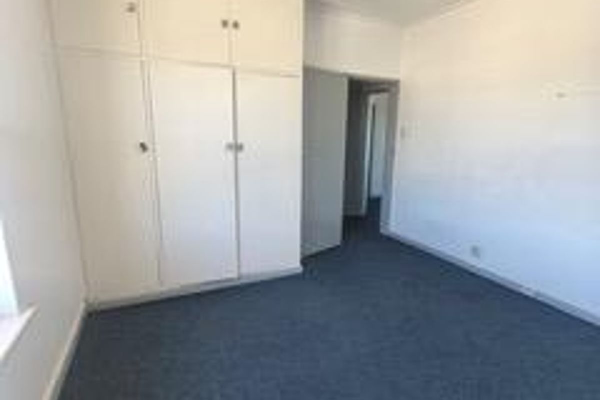 An empty bedroom featuring built-in cupboards, carpeted flooring, and a standard fluorescent light fixture, offering a blank canvas for renovation.