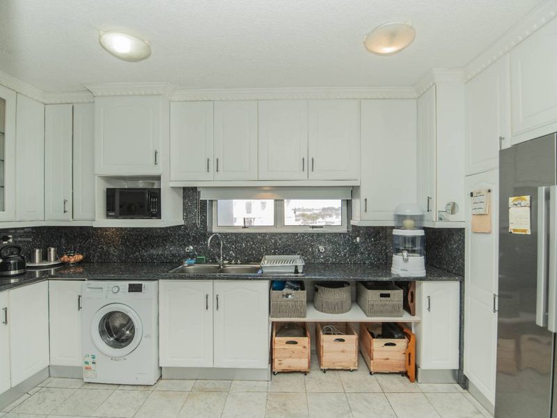 A functional kitchen featuring white cabinetry, dark granite countertops, a double basin sink, and integrated laundry facilities with tiled flooring.
