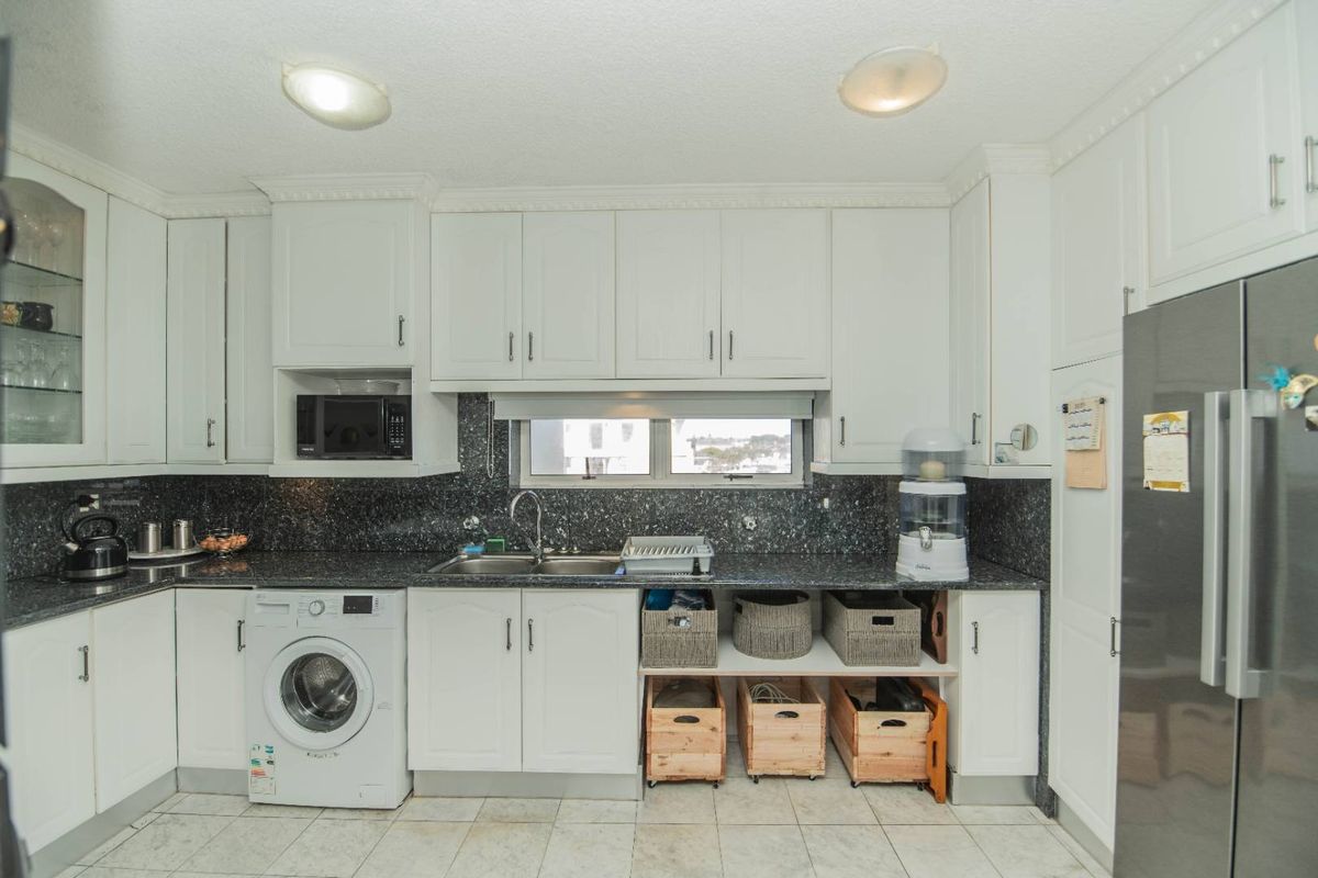 A functional kitchen featuring white cabinetry, dark granite countertops, a double basin sink, and integrated laundry facilities with tiled flooring.
