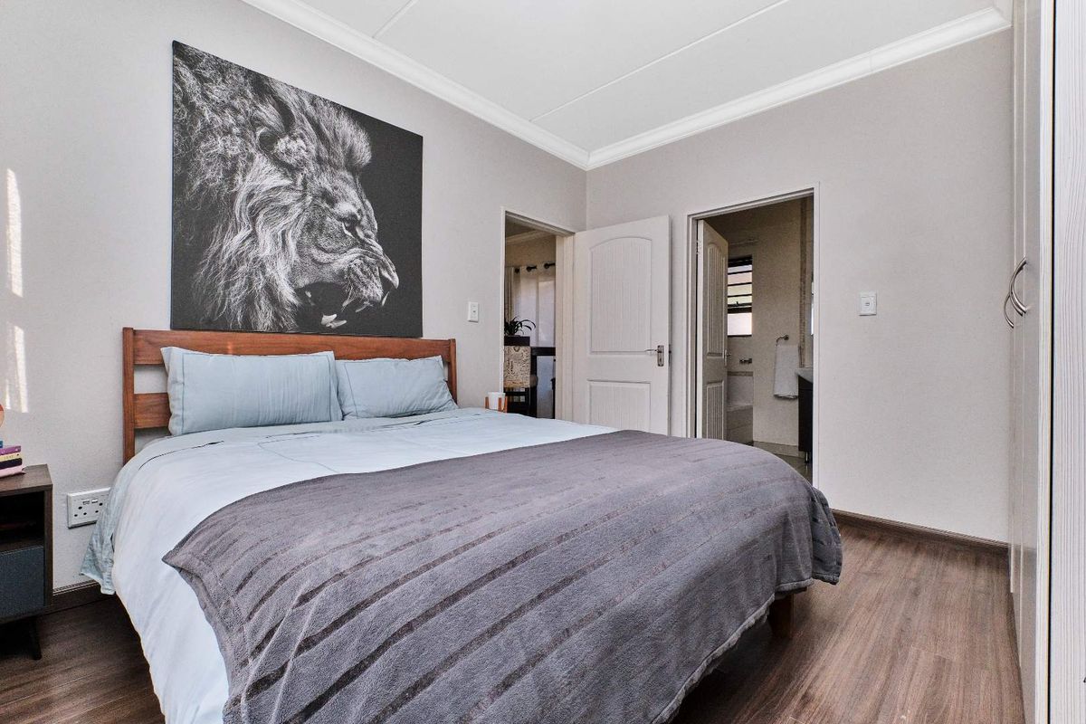 A well-maintained bedroom featuring wood-look flooring, crown molding, and an en-suite bathroom entrance.