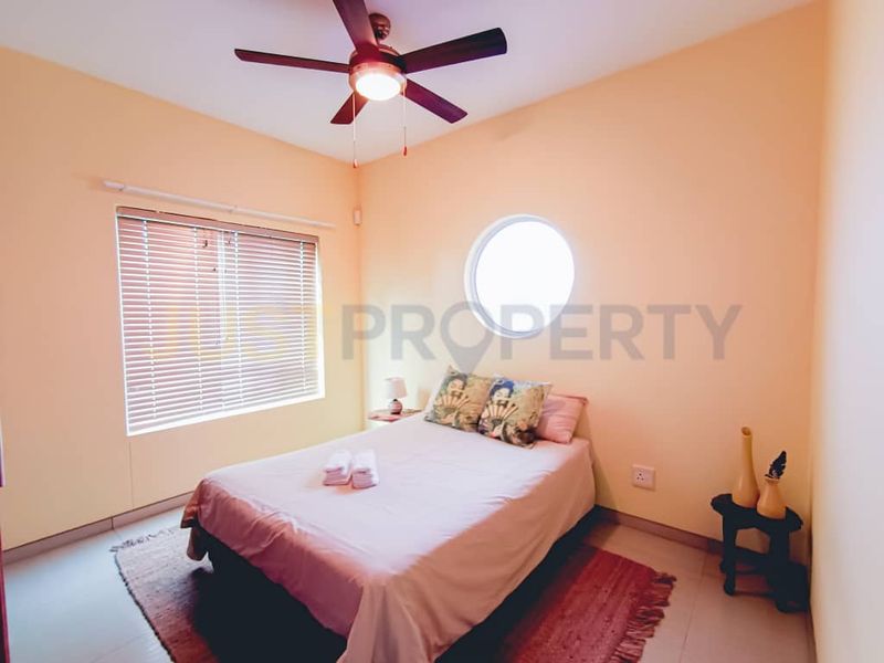 A bedroom featuring a ceiling fan, tiled flooring, and a distinctive circular window with venetian blinds.