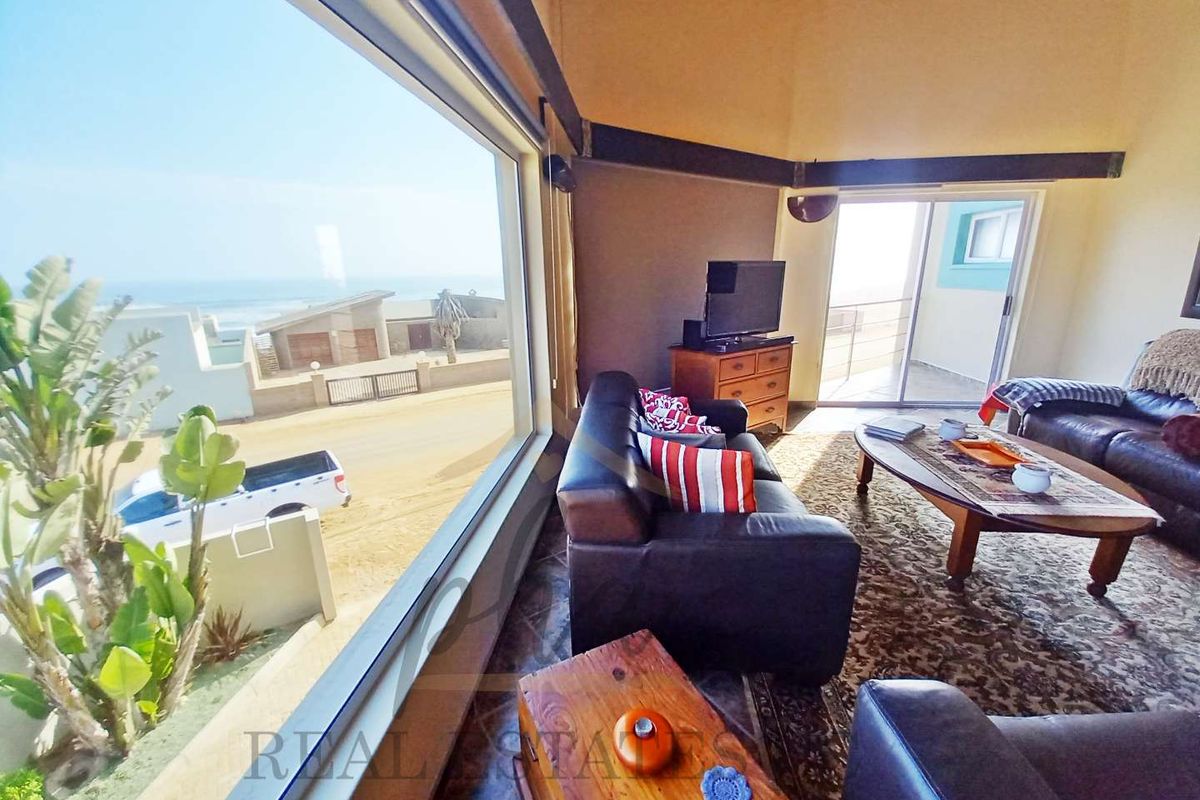 Spacious living area featuring high vaulted ceilings, exposed timber beams, and large picture windows offering expansive coastal views and access to a balcony.