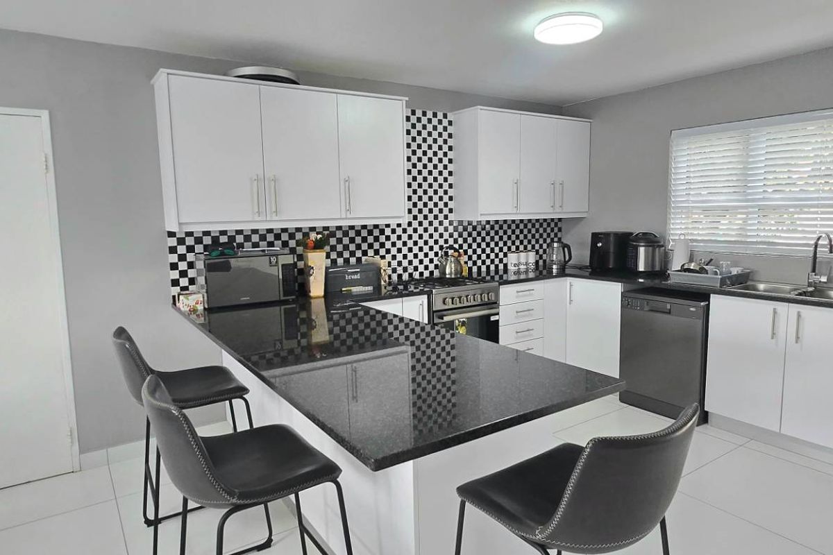 Modern kitchen featuring white cabinetry, contrasting black granite countertops, a distinctive checkered backsplash, and a functional breakfast bar island.