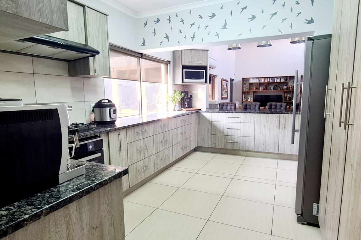 Modern kitchen featuring light wood-grain cabinetry, granite countertops, built-in appliances, and tiled flooring, with an open-plan layout connecting to the living area.