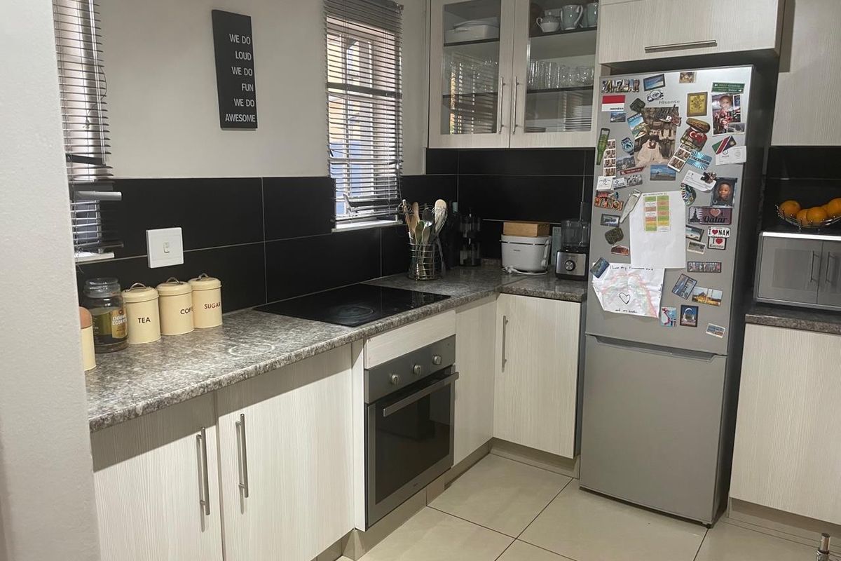 A functional kitchen featuring light wood-grain cabinetry, dark tiled backsplash, granite-look laminate countertops, and integrated electric cooking appliances.