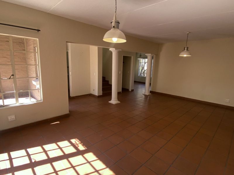 Spacious open-plan living area featuring terracotta floor tiles, decorative columns, and natural light through steel-framed windows.