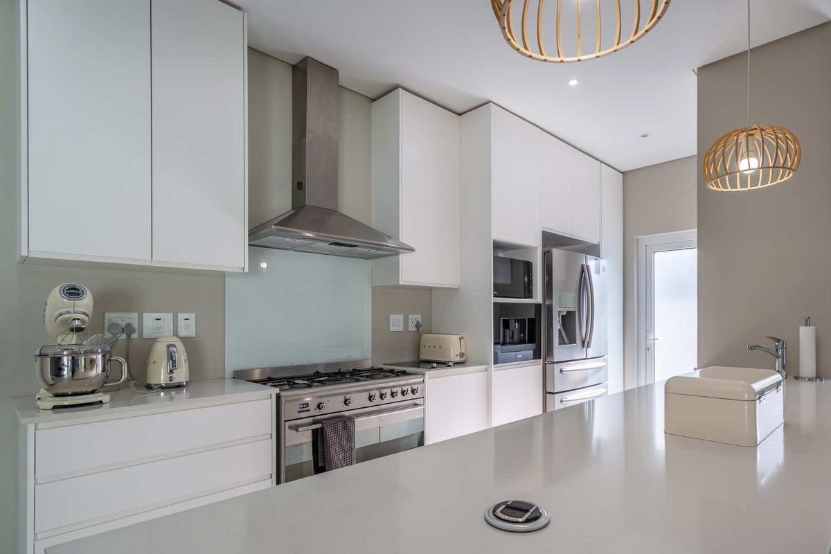 Modern kitchen featuring sleek white cabinetry, stone countertops, high-end stainless steel appliances, and a functional island with a pop-up power outlet.