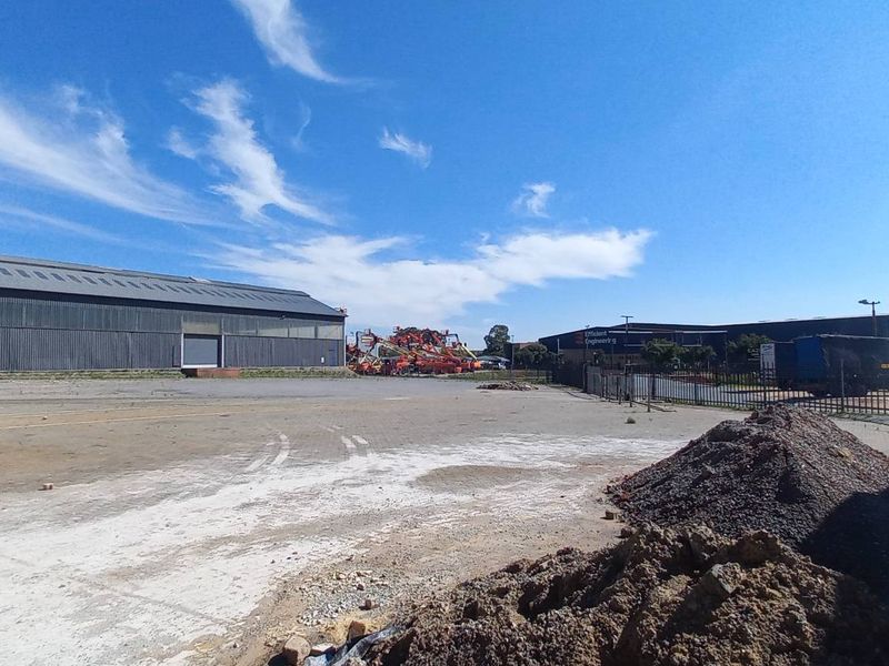 Expansive industrial yard area featuring a large warehouse structure, paved surfaces, and perimeter fencing, suitable for logistics or heavy equipment storage.