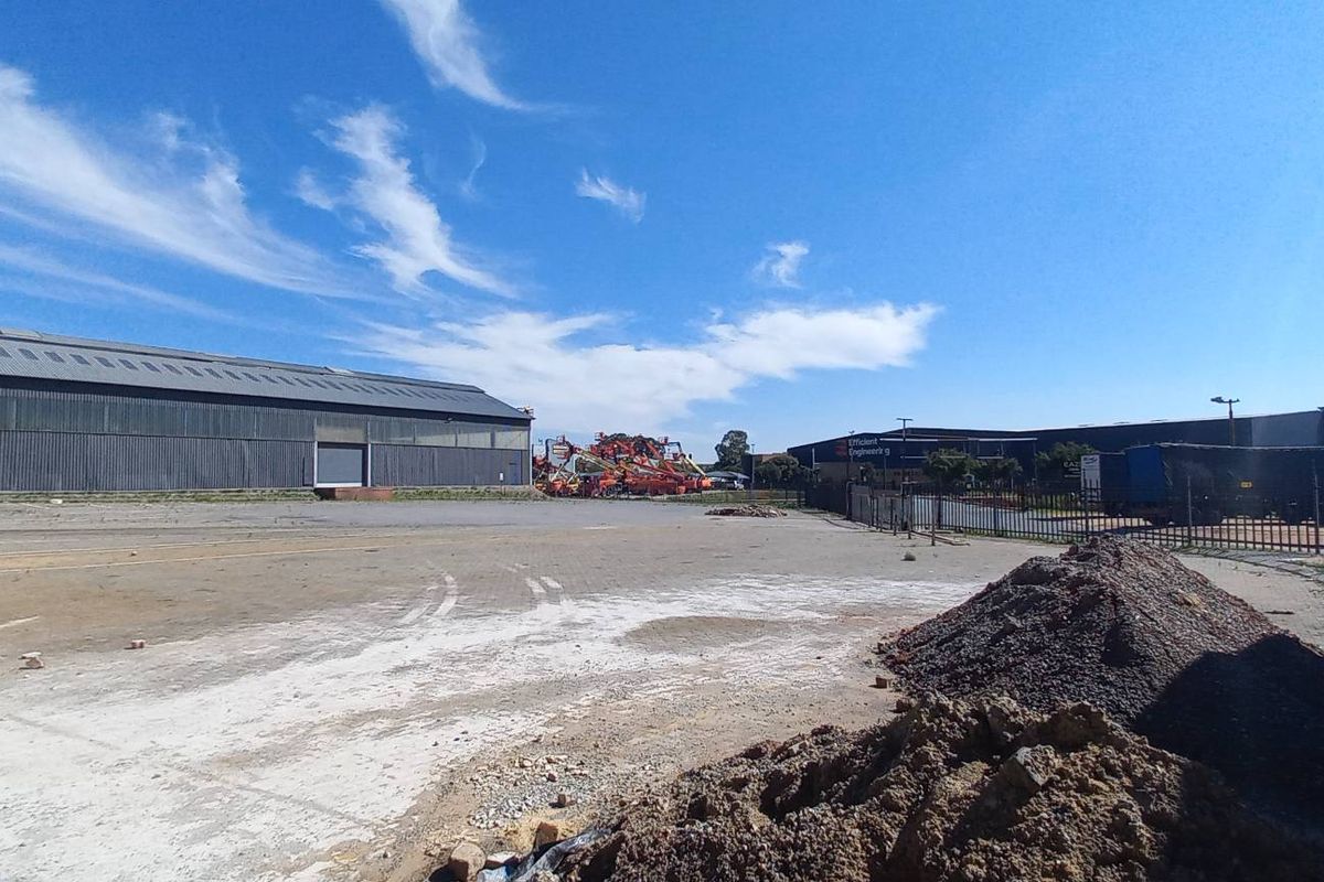 Expansive industrial yard area featuring a large warehouse structure, paved surfaces, and perimeter fencing, suitable for logistics or heavy equipment storage.