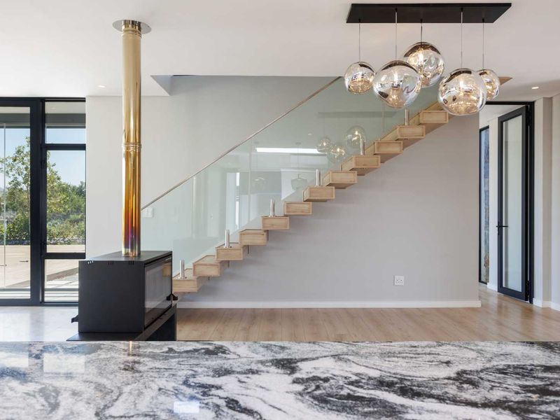 Modern open-plan living area featuring a striking floating staircase with glass balustrade, a sleek freestanding fireplace, and premium granite kitchen surfaces.