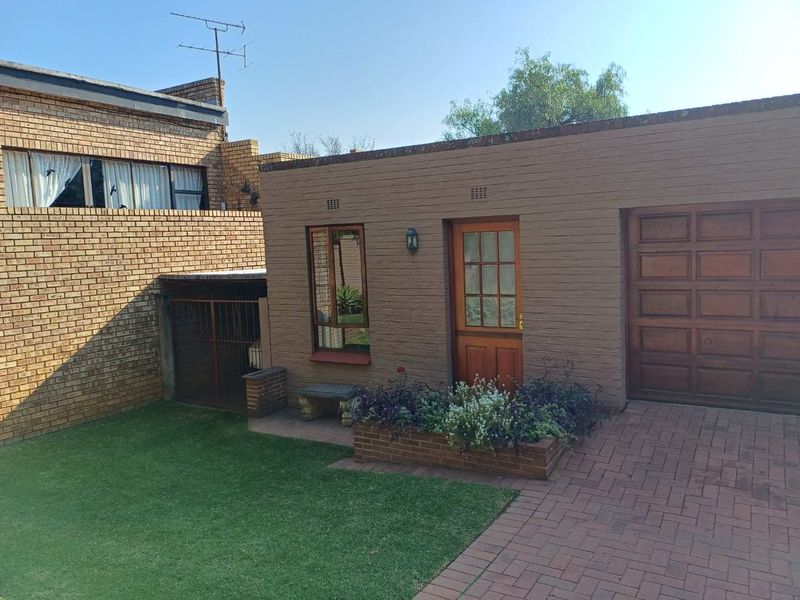 Rear exterior view of the cottage featuring a brick facade, integrated garage, timber entrance door, paved driveway, and a small garden area.