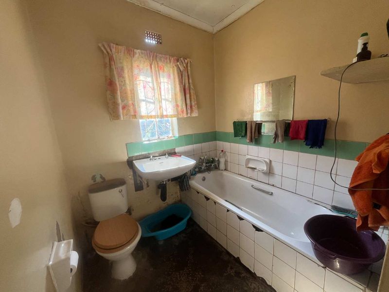 A dated bathroom featuring a standard bathtub, washbasin, and toilet with original wall tiling, requiring modernization and cosmetic updates.