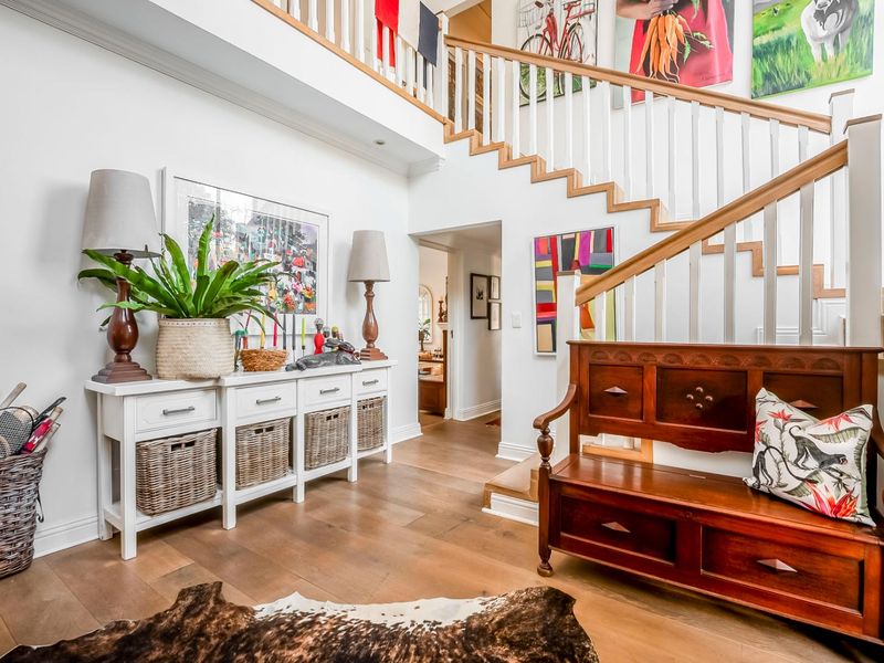 Spacious entrance foyer featuring a grand timber staircase, hardwood flooring, and a bright, open-plan layout leading into the home.