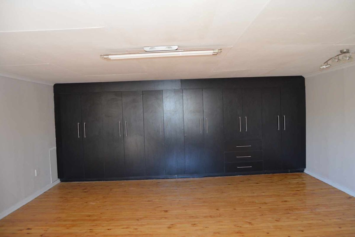 Spacious bedroom featuring extensive wall-to-wall built-in cabinetry with a dark finish and polished timber flooring.