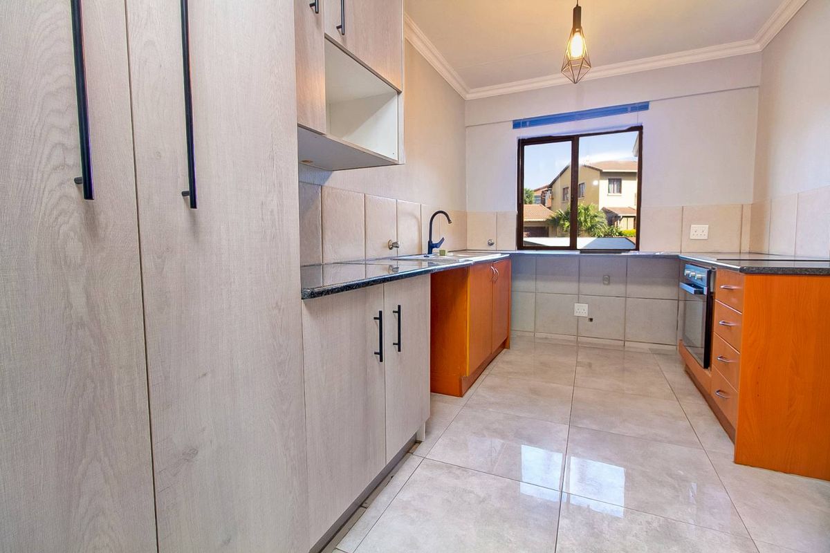 A functional kitchen featuring light wood-look cabinetry, dark granite countertops, tiled flooring, and a built-in oven with a hob.