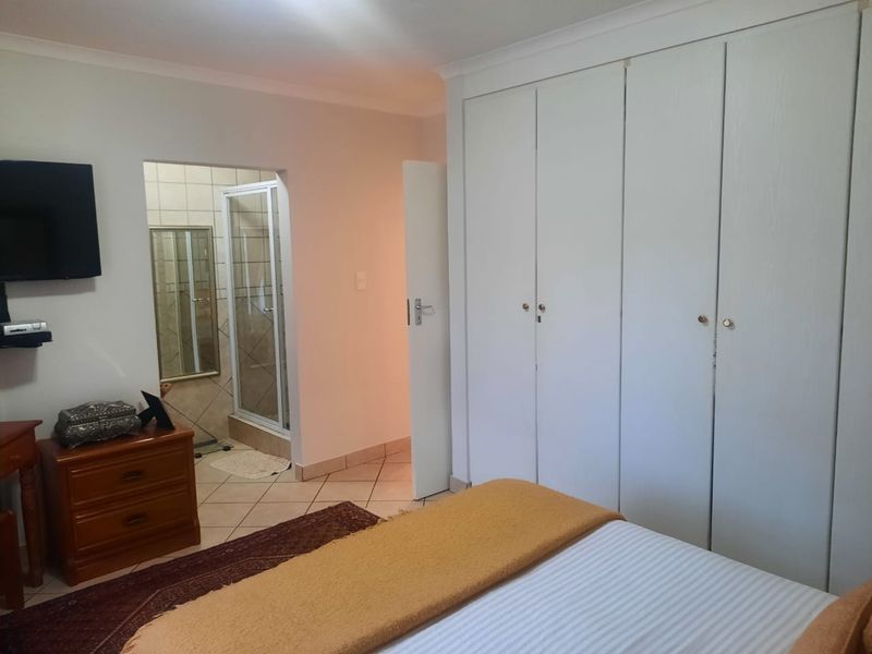 A bedroom featuring built-in cupboards and an adjoining en-suite bathroom with a shower enclosure, finished with neutral tiled flooring.