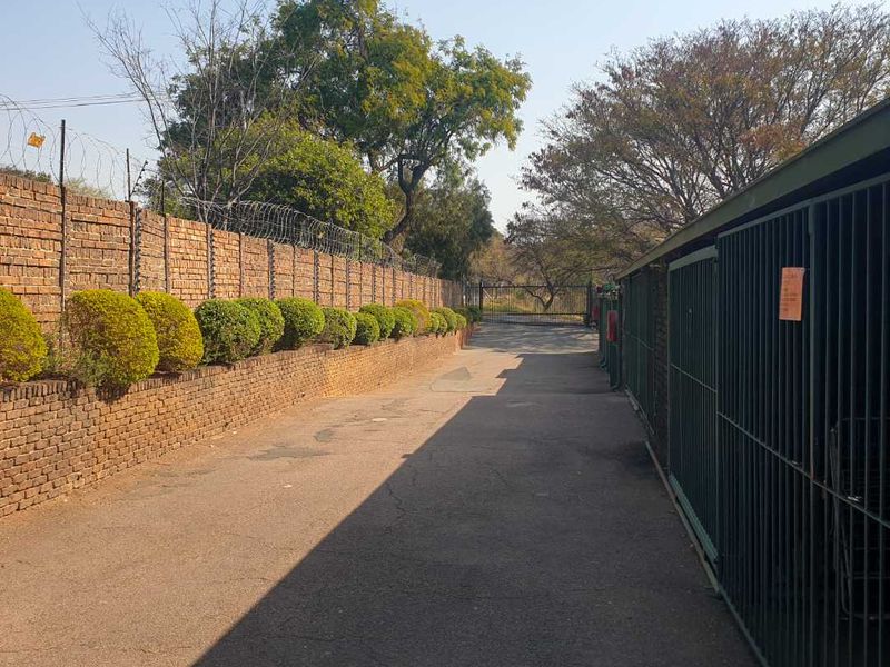 A paved driveway area featuring a high brick boundary wall with electric fencing and secure metal gate access.