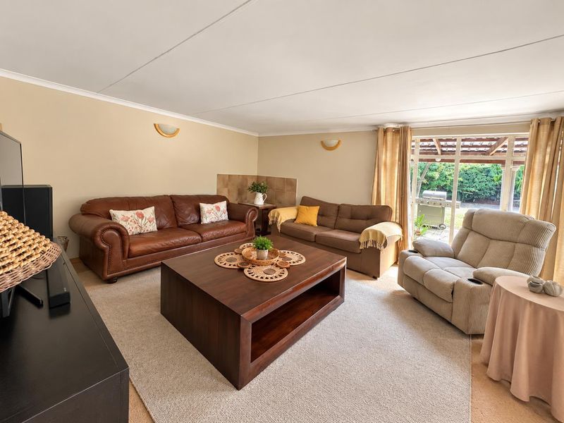 A comfortable living room featuring neutral walls, carpeted flooring, and a large sliding glass door providing direct access to the outdoor patio area.