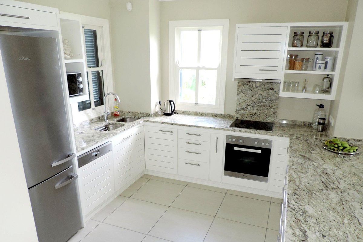 Modern kitchen featuring white cabinetry, granite countertops, integrated oven, hob, extractor fan, and stainless steel sink with tiled flooring.