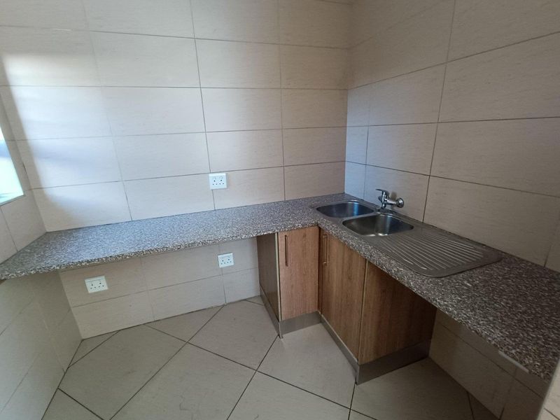 A clean and functional scullery area featuring wood-finish base cabinetry, a double bowl stainless steel sink, and durable granite-look laminate countertops with tiled finishes.