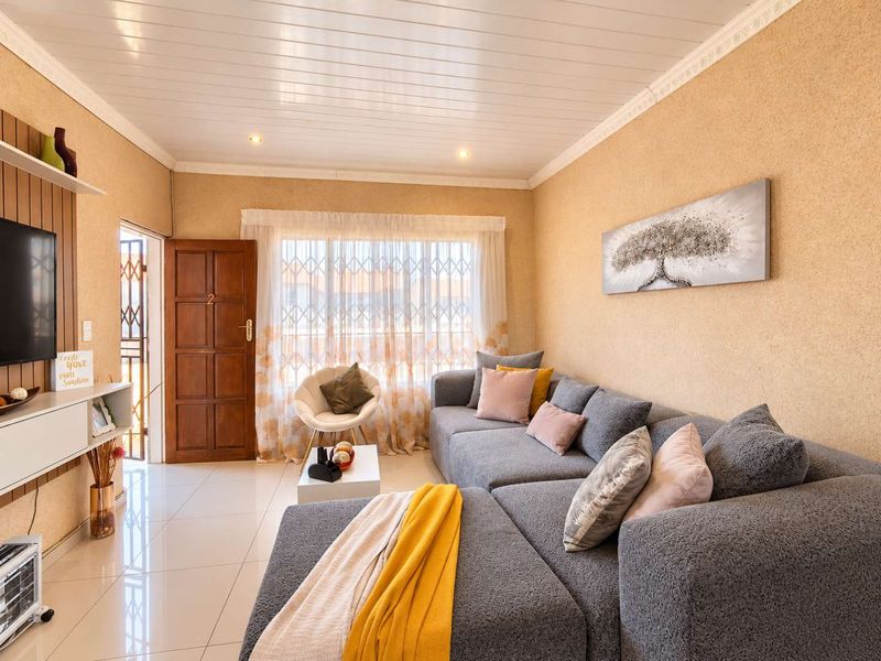 A well-lit living room featuring tiled flooring, textured walls, decorative ceiling cornicing, and a secure entrance door with an integrated security gate.