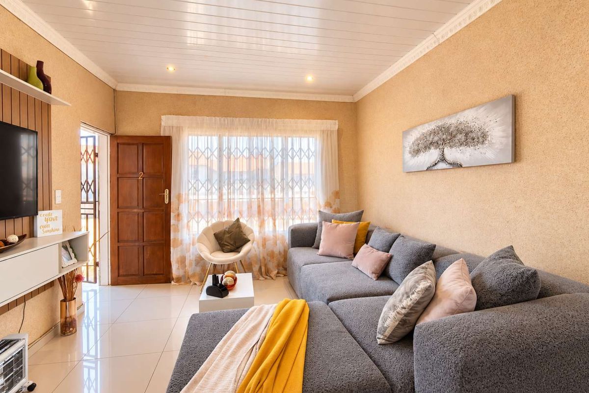 A well-lit living room featuring tiled flooring, textured walls, decorative ceiling cornicing, and a secure entrance door with an integrated security gate.