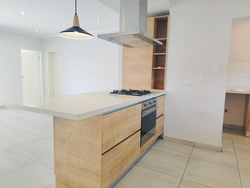 Modern kitchen featuring a central island with a gas hob, built-in oven, extractor fan, light wood cabinetry, and sleek stone countertops.