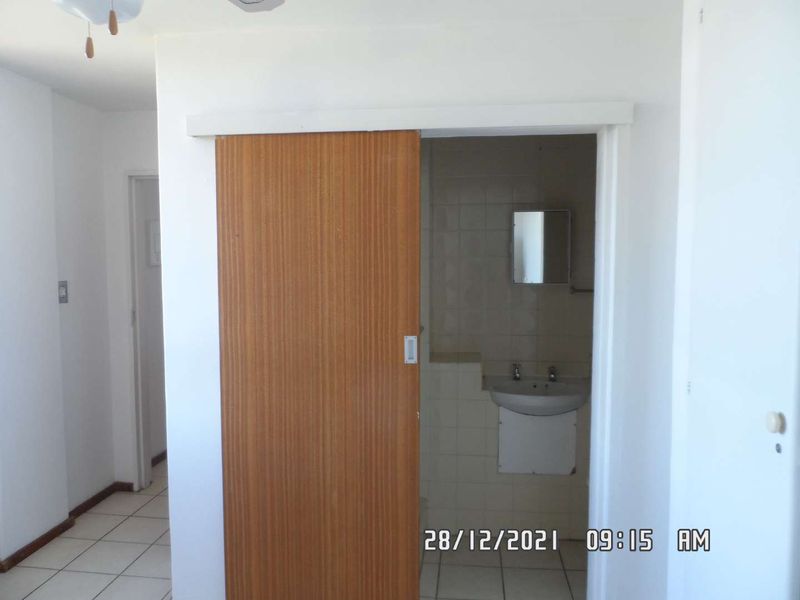 A functional bathroom featuring a wall-mounted basin, tiled finishes, and a sliding wooden door entry.