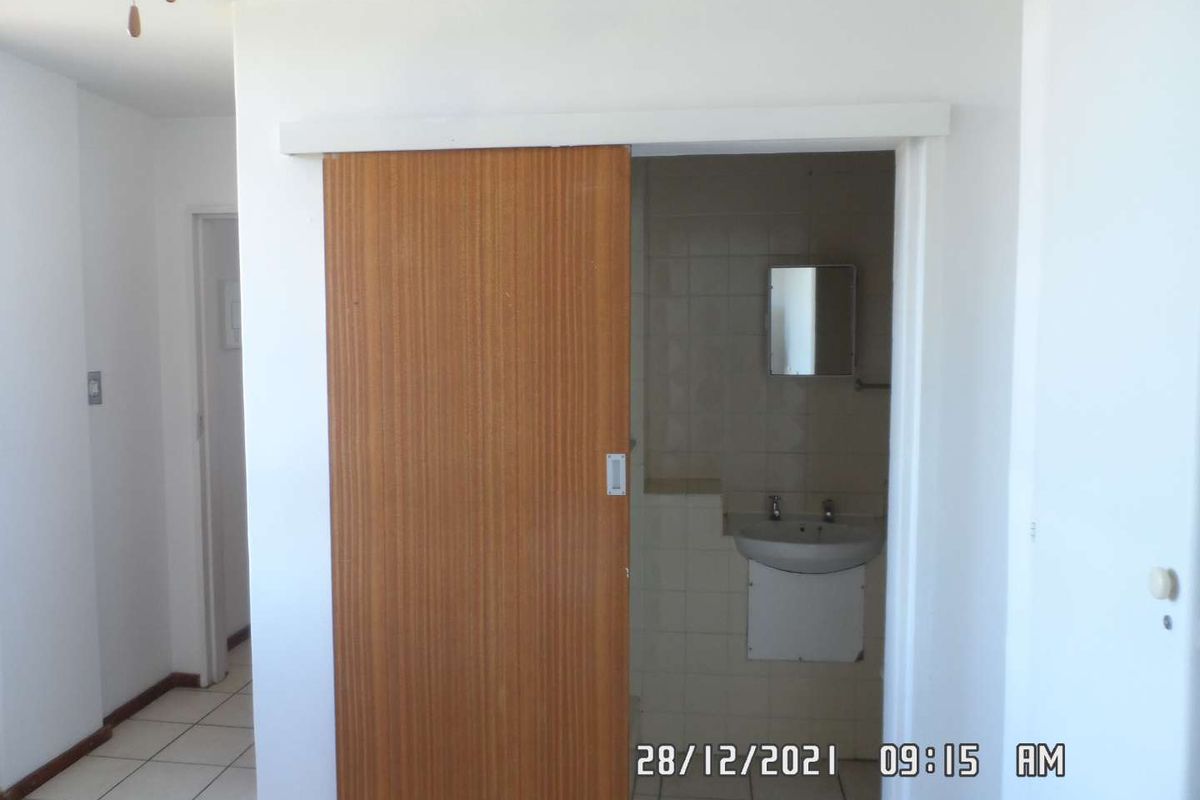 A functional bathroom featuring a wall-mounted basin, tiled finishes, and a sliding wooden door entry.