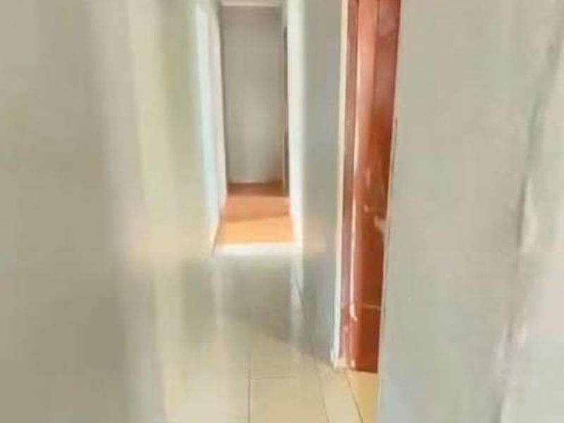 A narrow, empty hallway featuring tiled flooring and plain walls, providing access to adjacent rooms within the property.