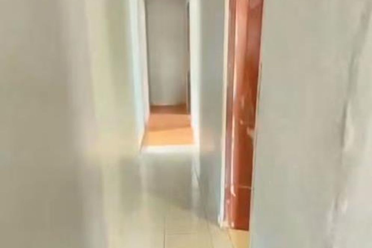 A narrow, empty hallway featuring tiled flooring and plain walls, providing access to adjacent rooms within the property.