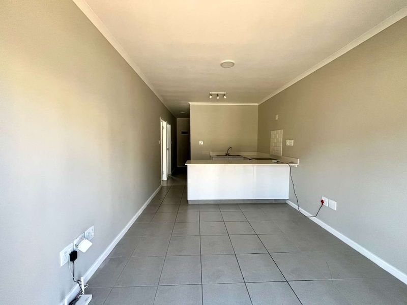 An open-plan living and kitchen area featuring neutral wall tones, tiled flooring, and a functional kitchen island with a built-in sink.