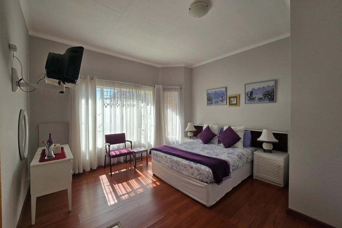 A well-lit bedroom featuring laminate flooring, a bay window with sheer curtains, and a built-in headboard design.