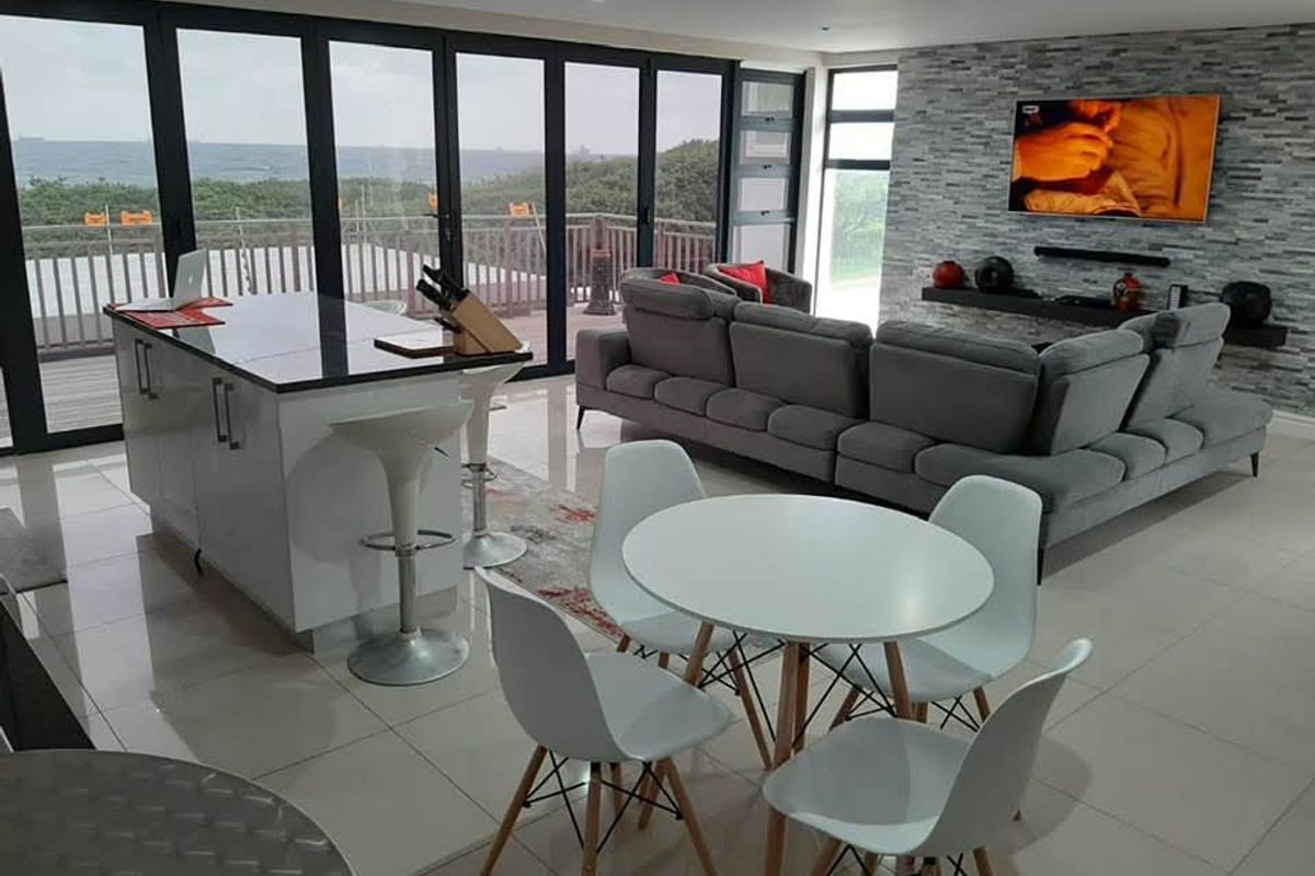 Modern open-plan living area featuring a kitchen island, stone feature wall, and expansive sliding glass doors offering scenic coastal views.