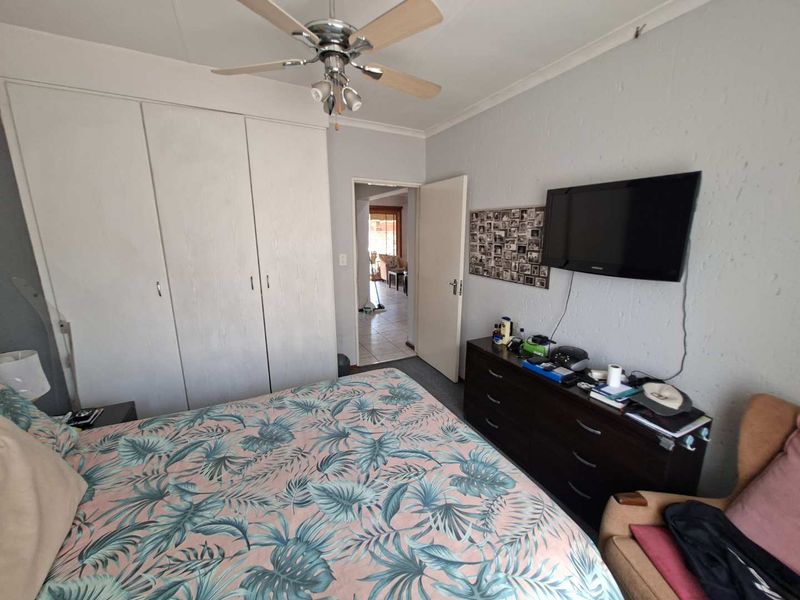 A functional bedroom featuring built-in cupboards and a ceiling fan, with direct access to the hallway.